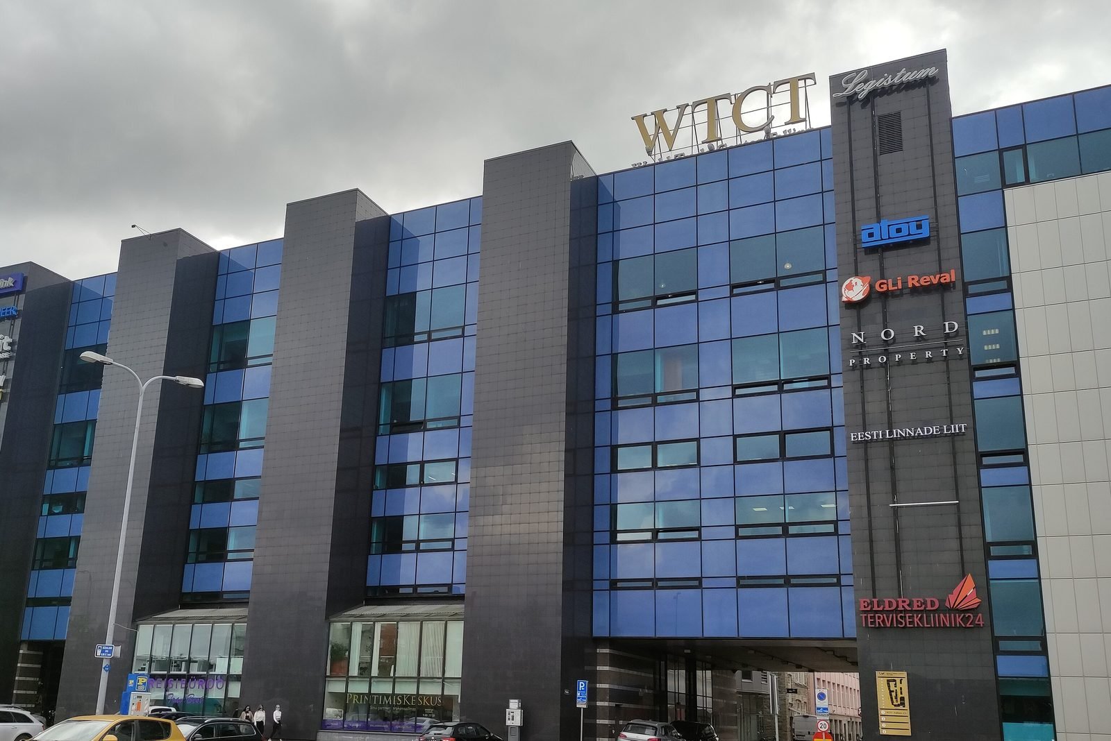 Street view of the World Trade Centre Tallinn: a six-storey building with a blue glass front and the nameplates of the companies based inside